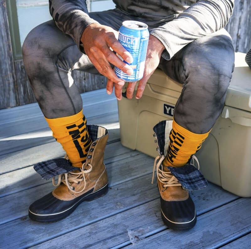 a man drinking a Montucky Cold Snack wearing Smartwool base layers and ski socks