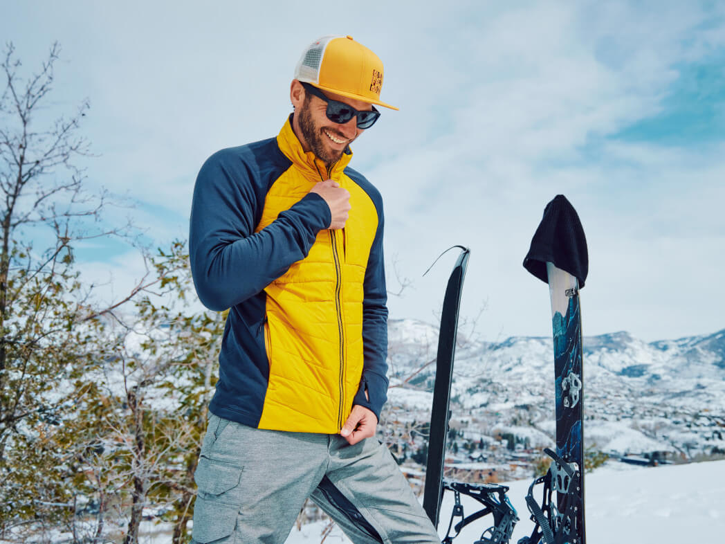 A man zipping up his Smartwool Mid Layer jacket outside in the cold