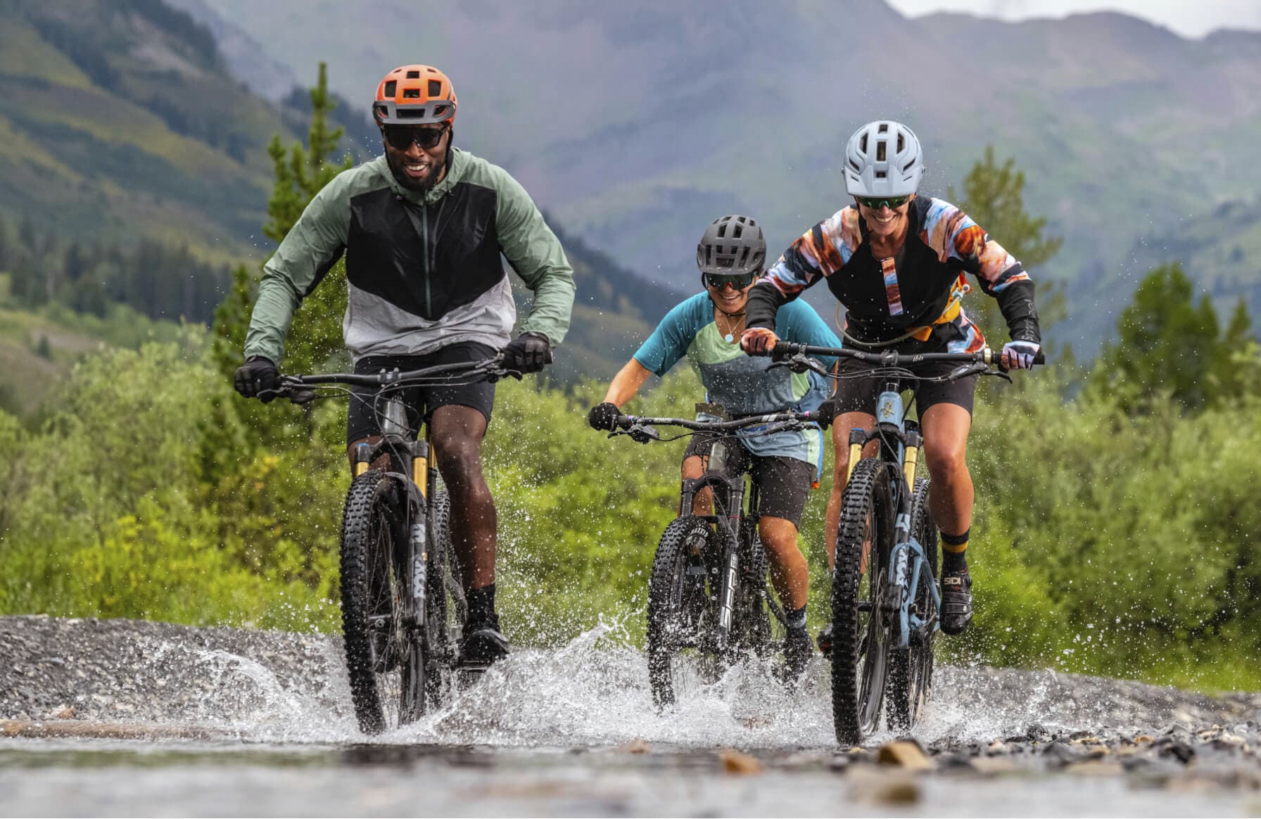 A group of people on their mountain bikes going through water wearing their Smartwool gear